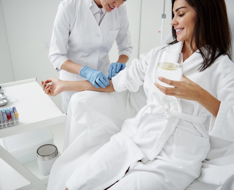 Doctor attaching intravenous drip on lady hand while she drinking water by Allure Aesthetics MD in SUGAR LAND, TX